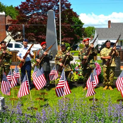 Honor guard in dress uniforms standing at a memorial surrounded by American flags